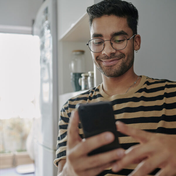 Smiling young man sitting in his kitchen and scrolling through his smart phone